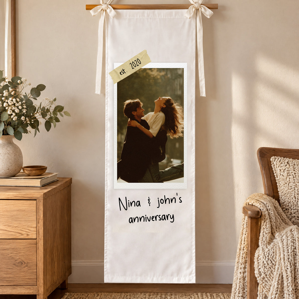 Personalized vertical photo party backdrop hanging on a wall from a wooden rod near a dresser and armchair