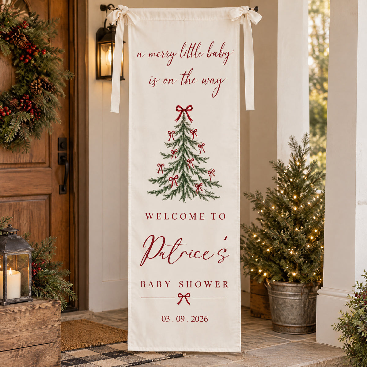 Personalized Christmas baby shower banner hanging on a porch beside a wreath, lantern and potted lit tree