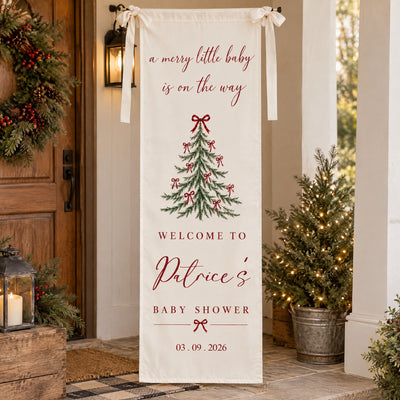 Personalized Christmas baby shower banner hanging on a porch beside a wreath, lantern and potted lit tree