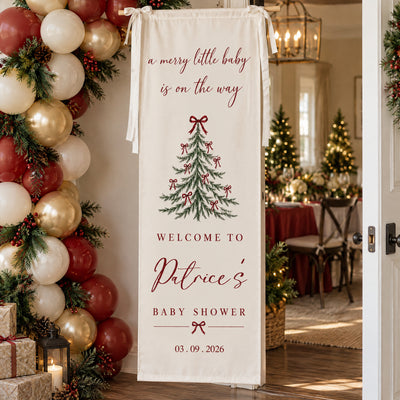 Personalized Christmas baby shower banner at a doorway beside red and gold balloon garland and a set table