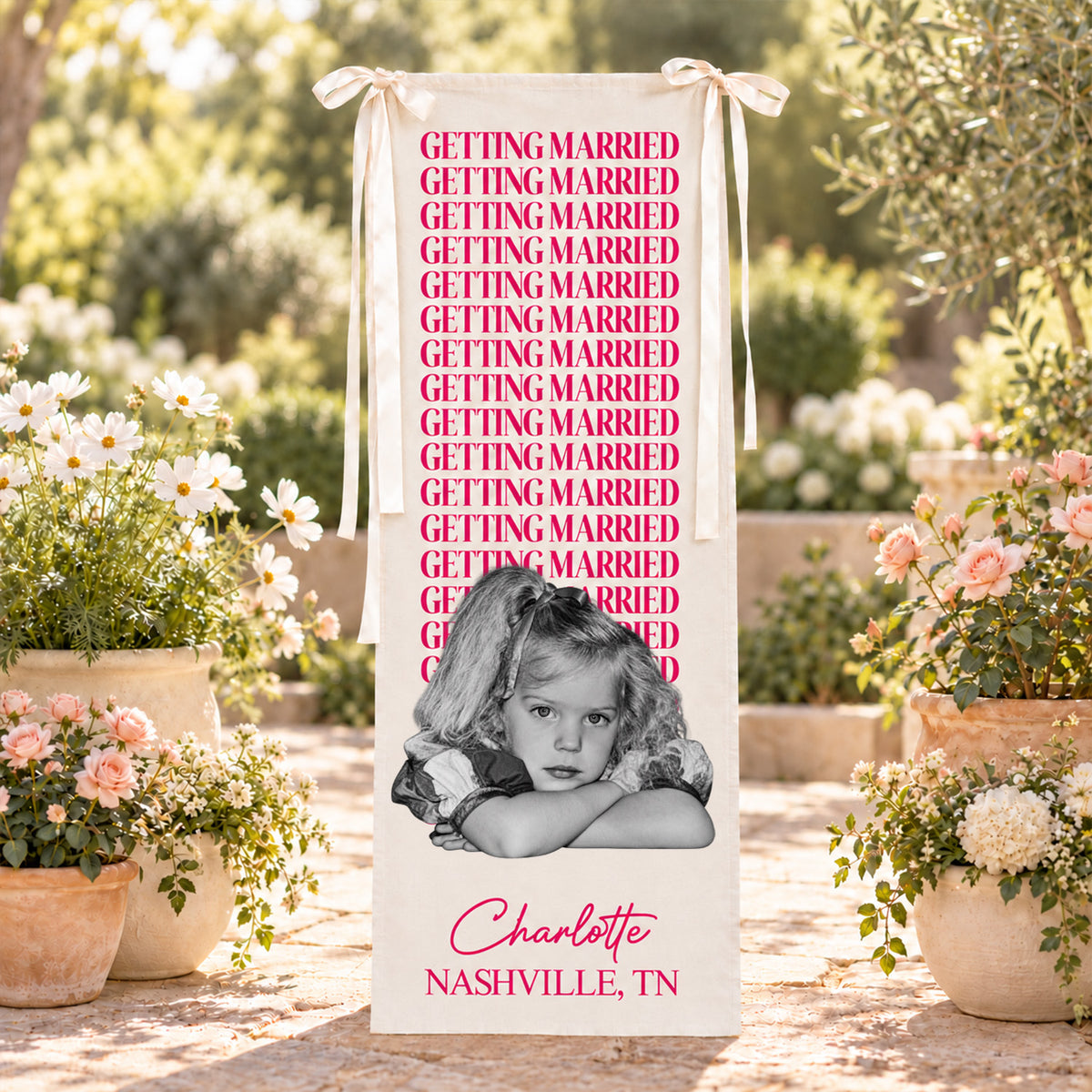 Personalized bachelorette party backdrop banner in pink hanging among potted flowers on a stone patio