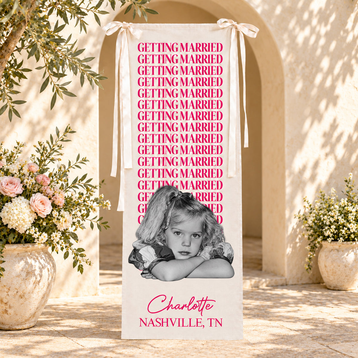 Personalized bachelorette party backdrop banner in pink in front of an arched doorway with vases of flowers