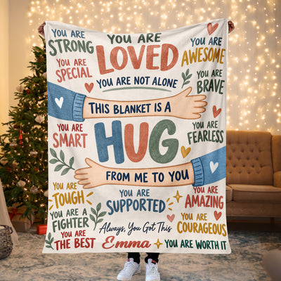 Personalized healing hug fleece blanket held up by a lit Christmas tree and string lights, name Emma shown