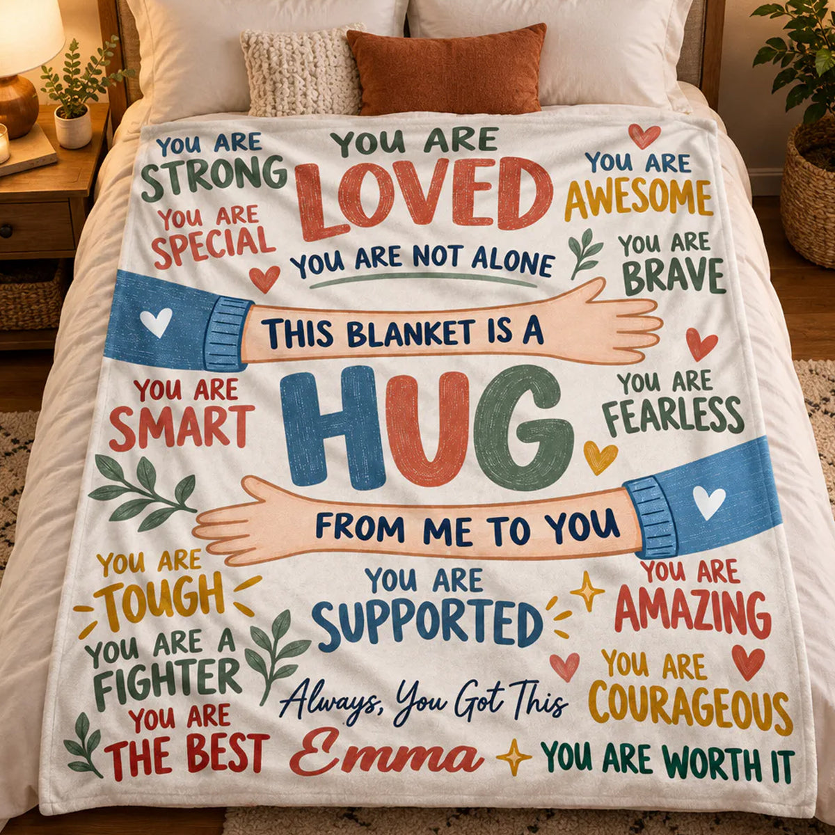 Personalized healing hug fleece blanket spread over a bed with pillows, seen from above, name Emma at bottom