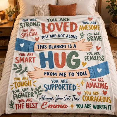 Personalized healing hug fleece blanket held up by a lit Christmas tree and string lights, name Emma shown