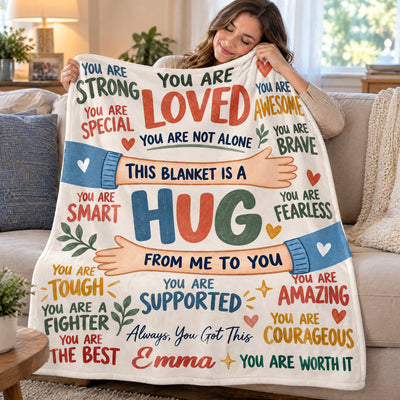 Personalized healing hug fleece blanket held by a smiling woman resting her cheek on it, seated on a sofa