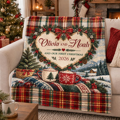 Our First Christmas Personalized Blanket draped over a cream sofa beside a lit tree and fireplace