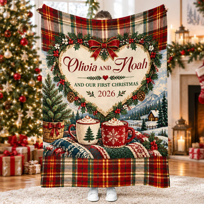 Our First Christmas Personalized Blanket draped over a cream sofa beside a lit tree and fireplace