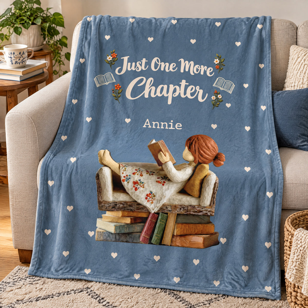 Personalized Blanket in blue draped over a beige armchair, showing a girl reading on a sofa of books with the name Annie