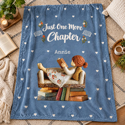 Personalized Blanket in blue laid flat on a rug beside an open book, a cup of coffee and a knit throw