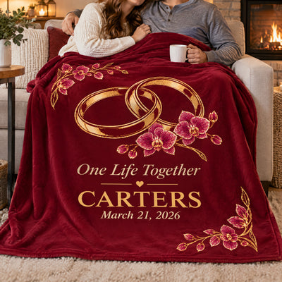 Personalized wedding rings blanket covering a couple on a sofa beside a fireplace, one holding a white mug