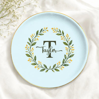 Monogram botanical wreath custom ceramic dish in light blue with Taylor name, gold rim, on white fabric beside baby's breath