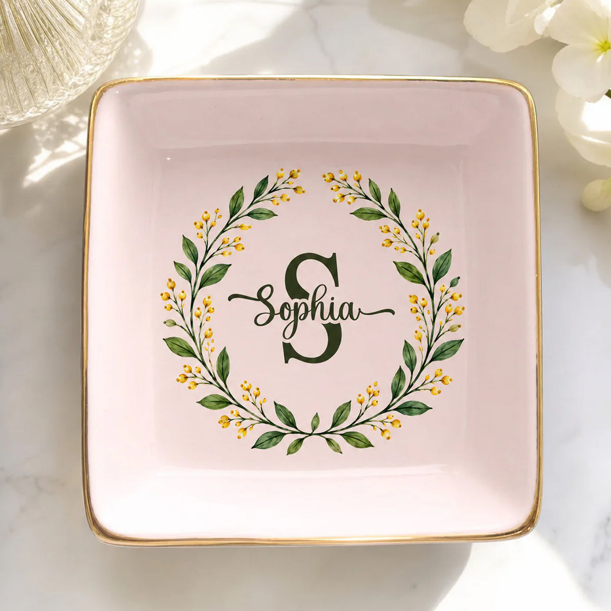 Monogram botanical wreath custom ceramic dish, square pink with Sophia and gold rim, on marble beside white flowers