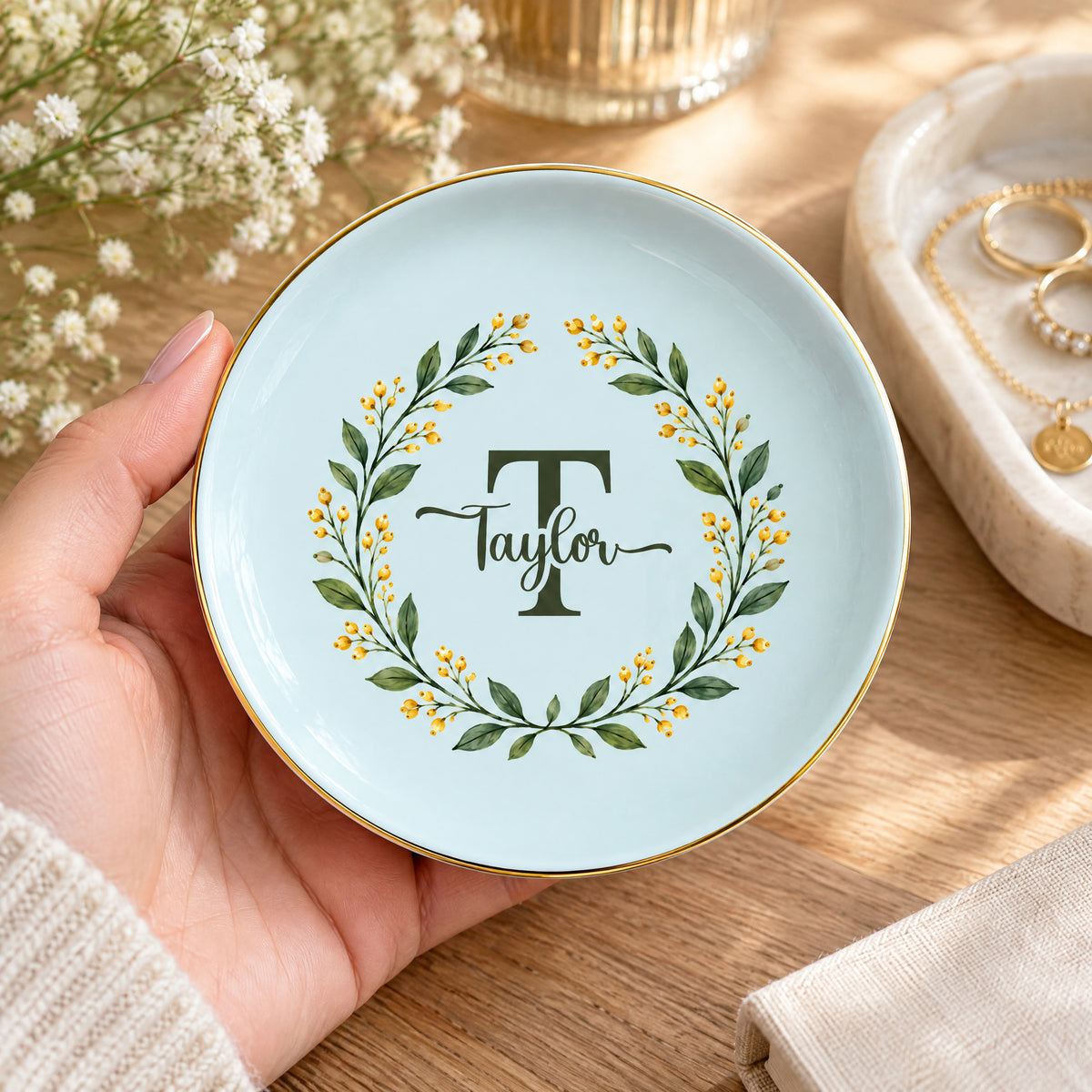 Monogram botanical wreath custom ceramic dish in light blue held in a hand, with rings and a necklace on a tray nearby