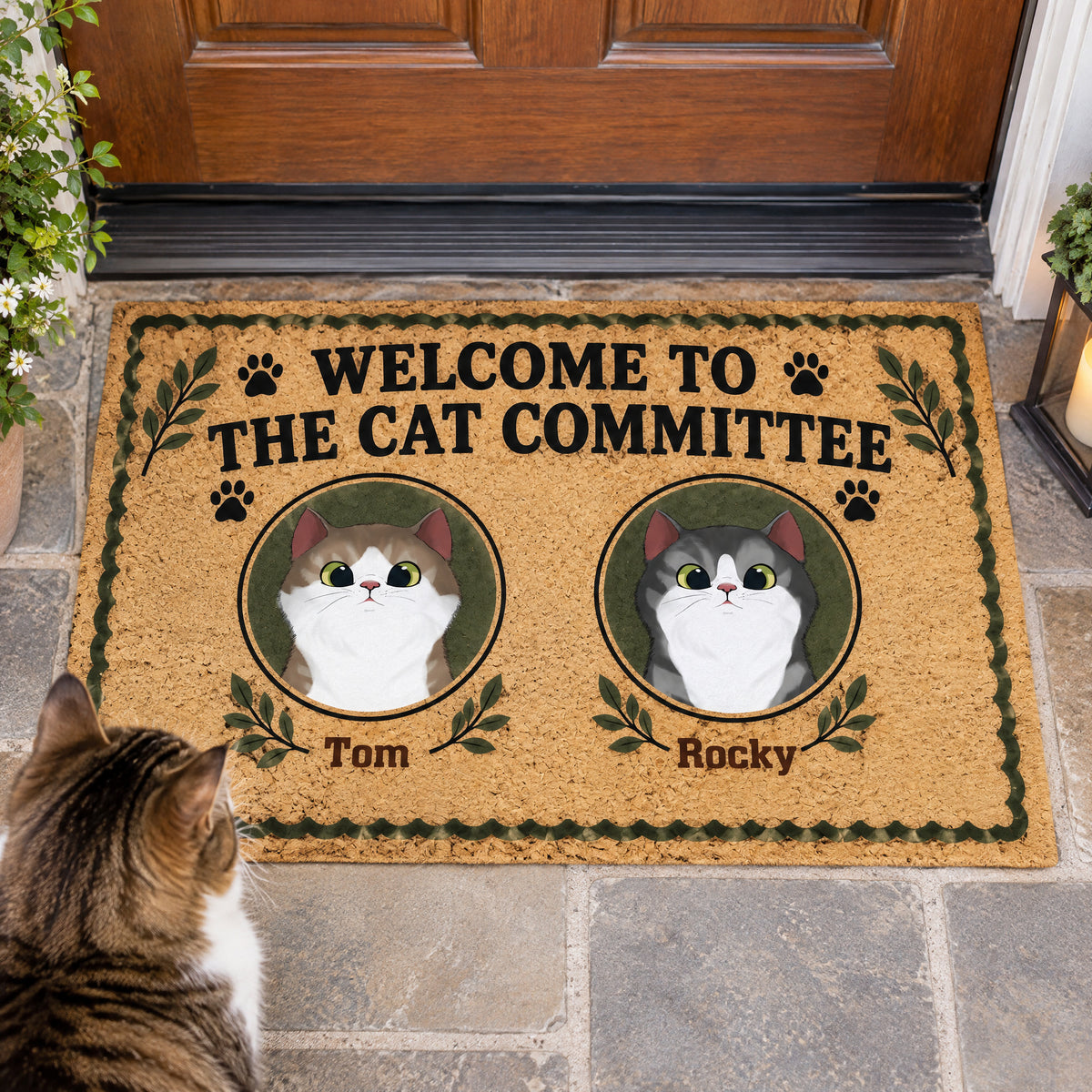 Personalized Cat Committee Doormat with two cat portraits named Tom and Rocky, real cat sitting beside it