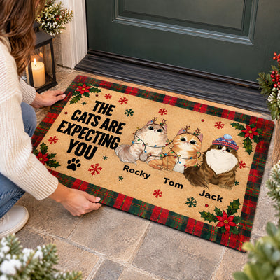 Personalized cat doormat being straightened by a person in a cream sweater beside a lit lantern