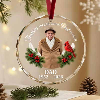 Personalized glass ornament custom photo hanging on red ribbon beside pine branch and pinecone