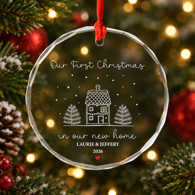 Personalized glass ornament new home in close view hanging among pine branches, red baubles and glowing lights