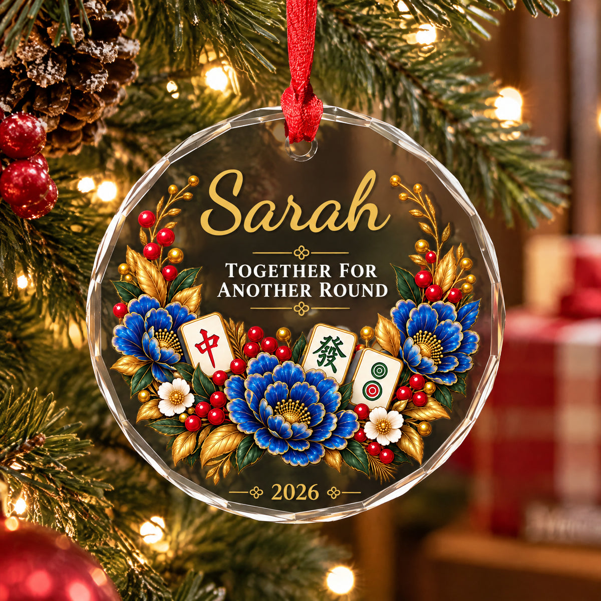 Personalized glass ornament with mahjong hanging among pine branches, pinecones and red baubles, with gold leaves