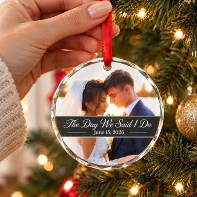 Personalized glass ornament custom photo held by a hand on a red ribbon in front of a lit tree