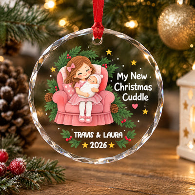 Personalized glass ornament My New Christmas Cuddle on a wooden table beside a pinecone and gold bauble