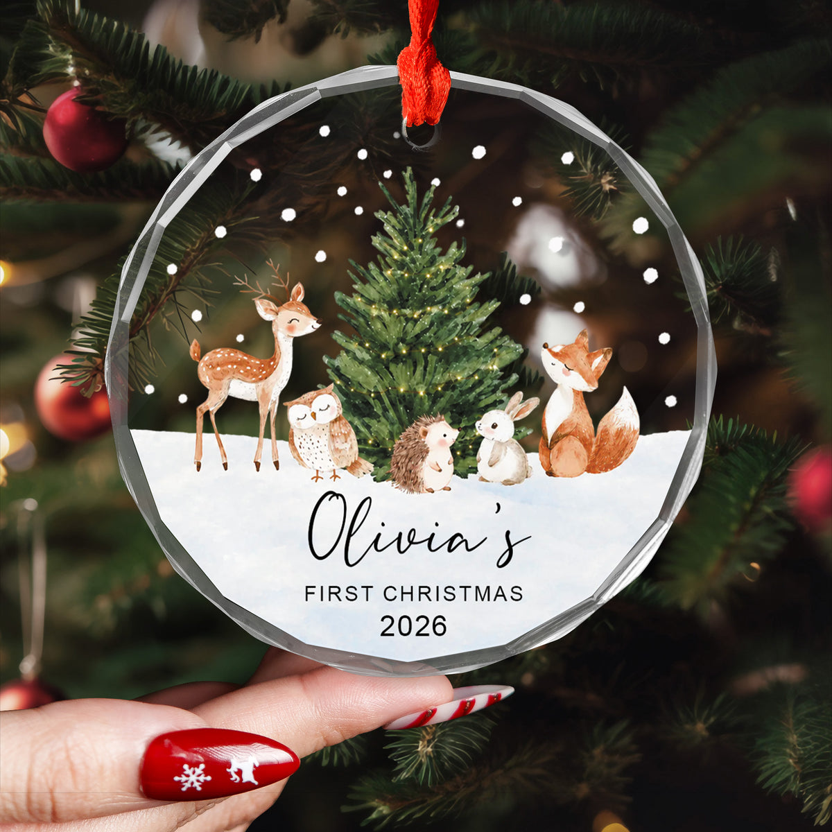 Personalized Woodland Animals Glass Ornament held in a hand with red nails in front of a decorated tree