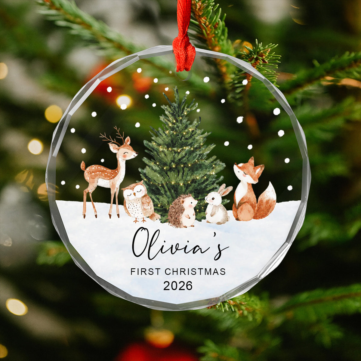 Personalized Woodland Animals Glass Ornament hanging on a red ribbon against blurred tree lights