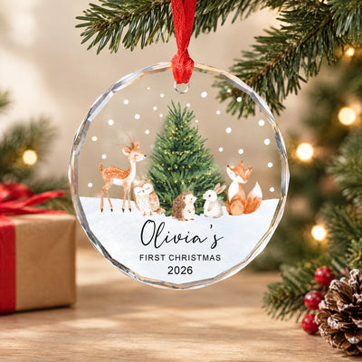 Personalized Woodland Animals Glass Ornament hanging on a branch near a wrapped gift, red berries and a pinecone