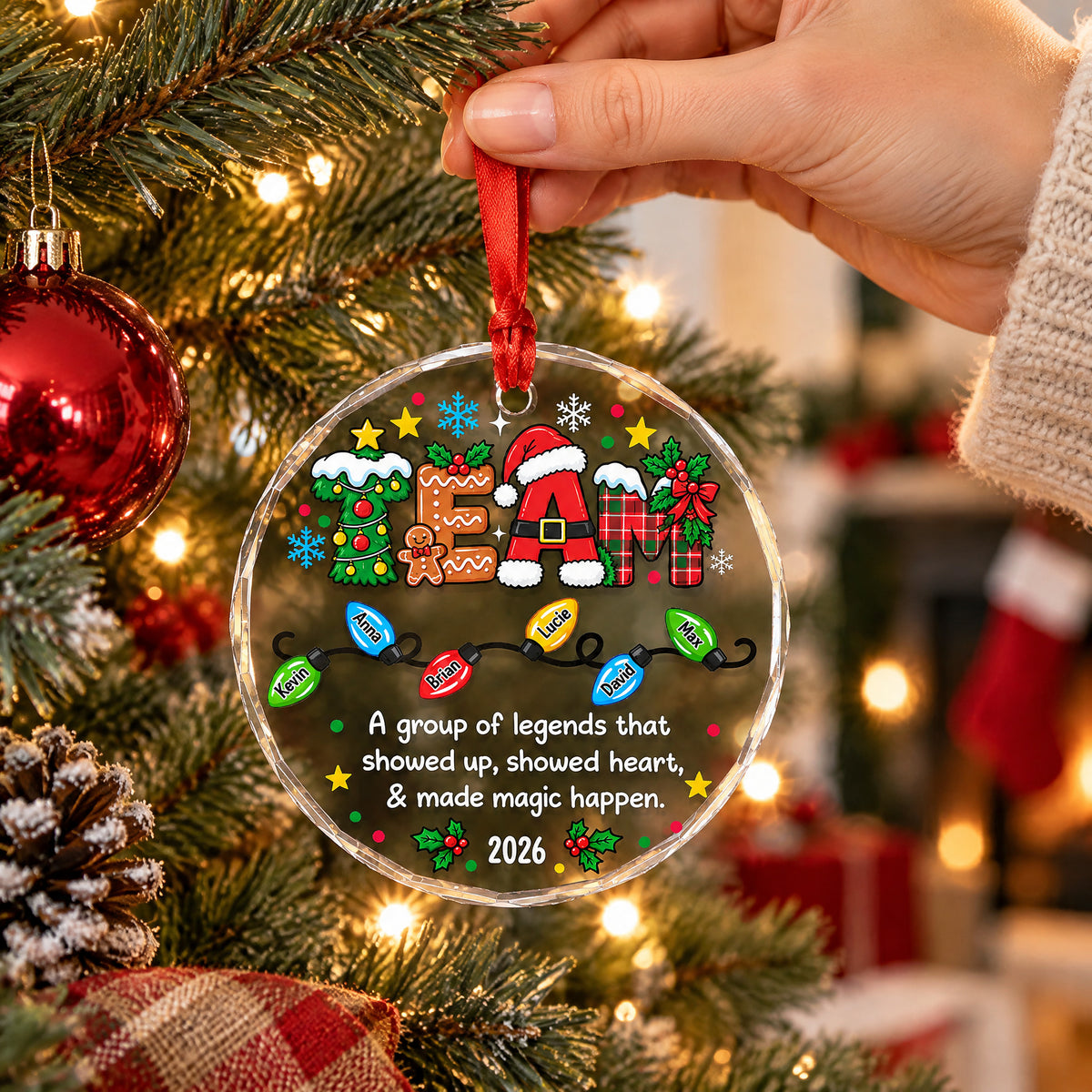 Personalized glass ornament custom team held up by hand near tree branches, a red stocking in the background