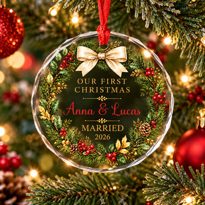 Personalized glass ornament first Christmas married hanging on a lit tree beside a red bauble, wreath and bow design