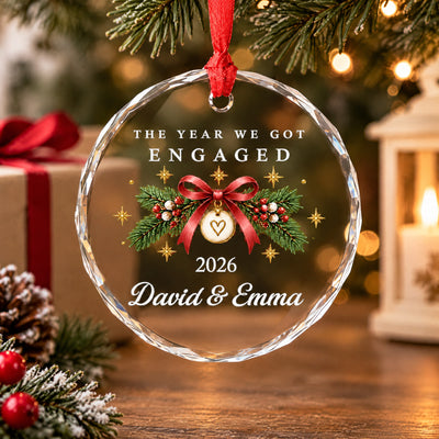 Personalized Glass Ornament Engaged Couple on a table with a wrapped gift, a lit candle lantern and snowy pine