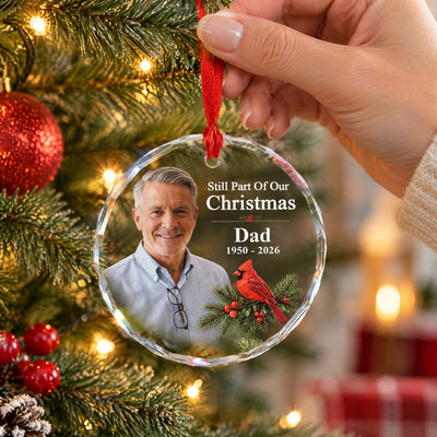Personalized glass ornament custom photo held by its red ribbon beside tree lights and red baubles