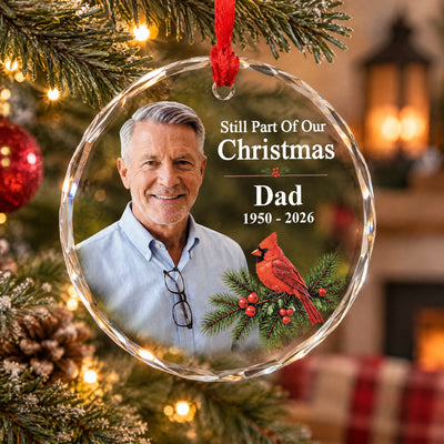 Personalized glass ornament custom photo hanging on a tree with a pine cone and a fireplace glowing behind