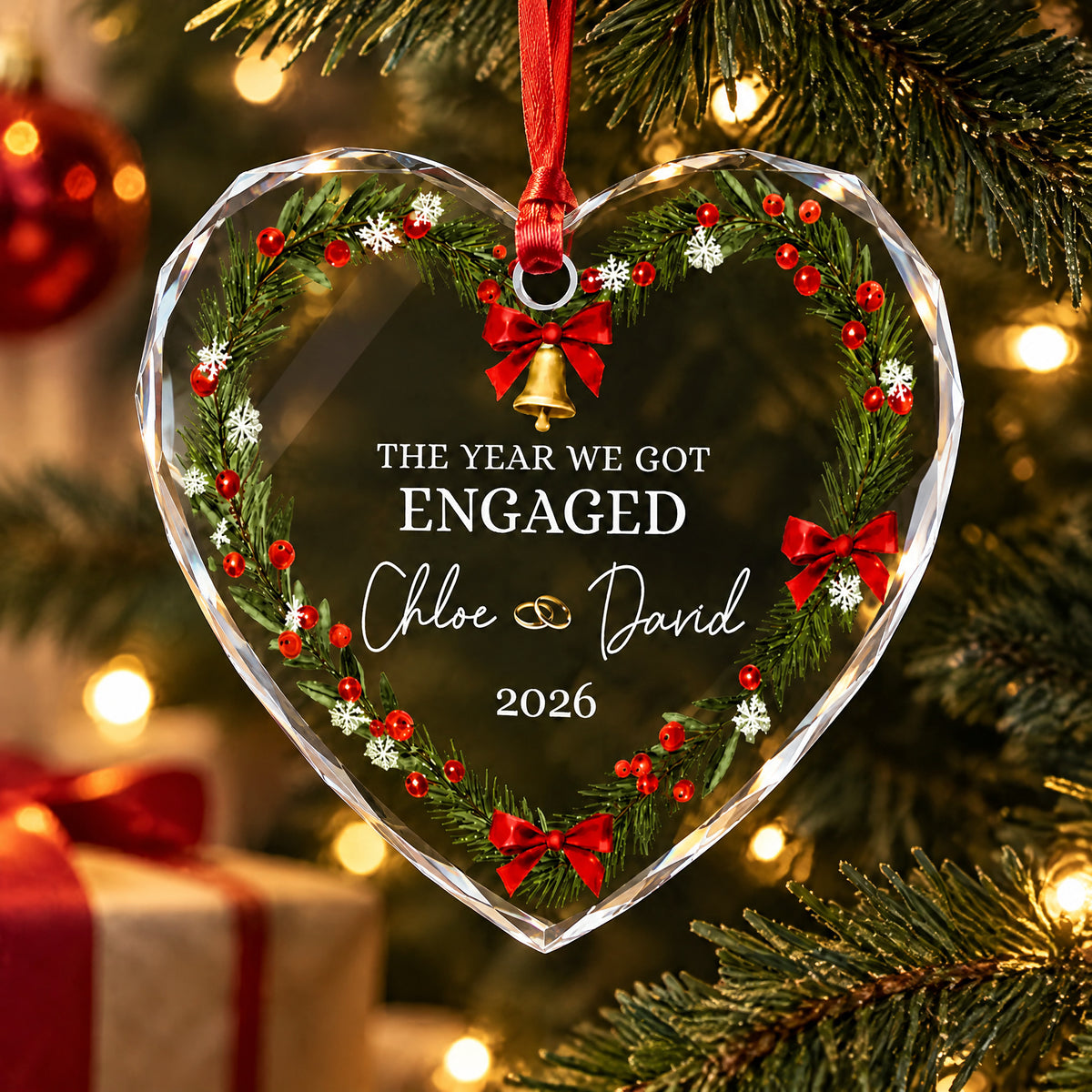 Personalized glass ornament hanging from red ribbon on a lit tree with a wrapped gift in the background