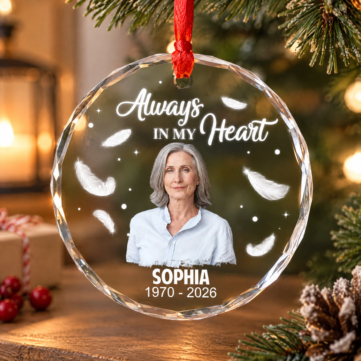 Personalized Glass Ornament Always In My Heart hanging on a tree with candle, gift box and pinecone, woman's photo shown