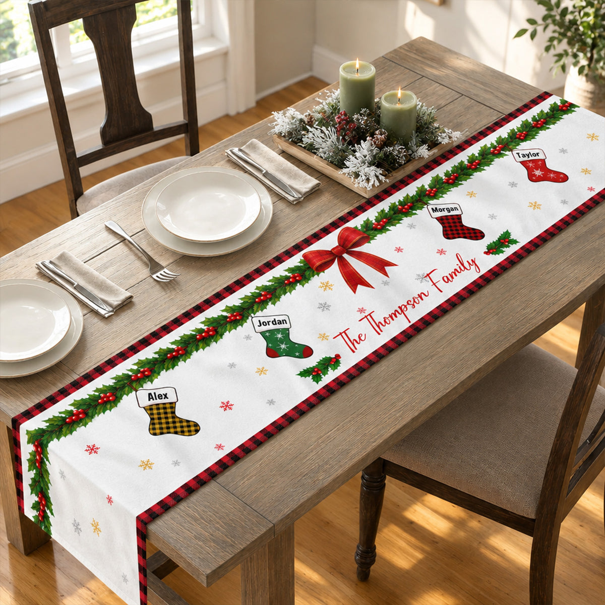 Personalized Christmas table runner on a wooden table with place settings and candles in a greenery centerpiece