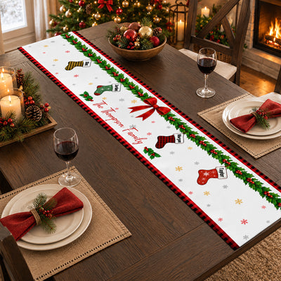 Personalized Christmas table runner on a dark table with woven placemats, red napkins and an ornament bowl