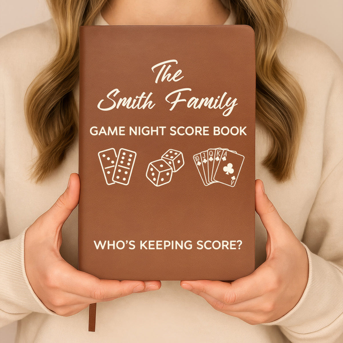 Personalized leather journal game night score held upright in both hands by a person in a cream sweater