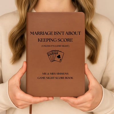 Personalized leather journal score book held upright in both hands against a cream sweater, playing cards design on cover