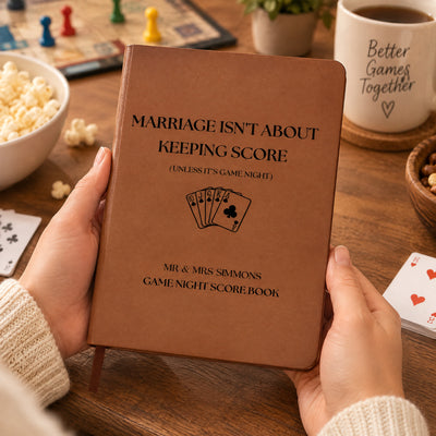 Personalized leather journal score book held over a table with popcorn, board game pieces, a mug and playing cards