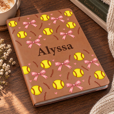 Personalized softball pattern leather journal lying on a wooden table beside a coffee cup and knit blanket