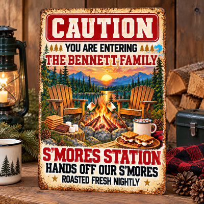 Personalized metal sign S’mores Station standing on a wooden shelf beside a lantern and stacked firewood