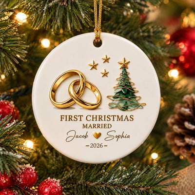 Personalized First Christmas Married Ceramic Ornament with gold rings and tree beside a gift and pinecone on a wooden table