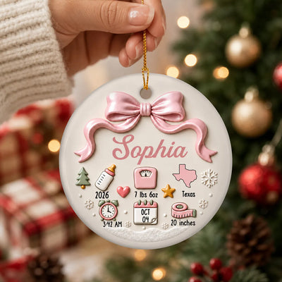 Personalized Baby Birth Details Christmas Ornament in pink with bow, held by a hand in front of a lit tree