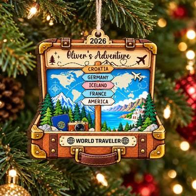 Personalized suitcase wooden ornament held by a hand in front of a lit Christmas tree with red baubles