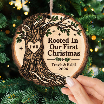 Personalized Wooden Ornament Rooted In Our First Christmas held by hand near snowy pinecones and red berries