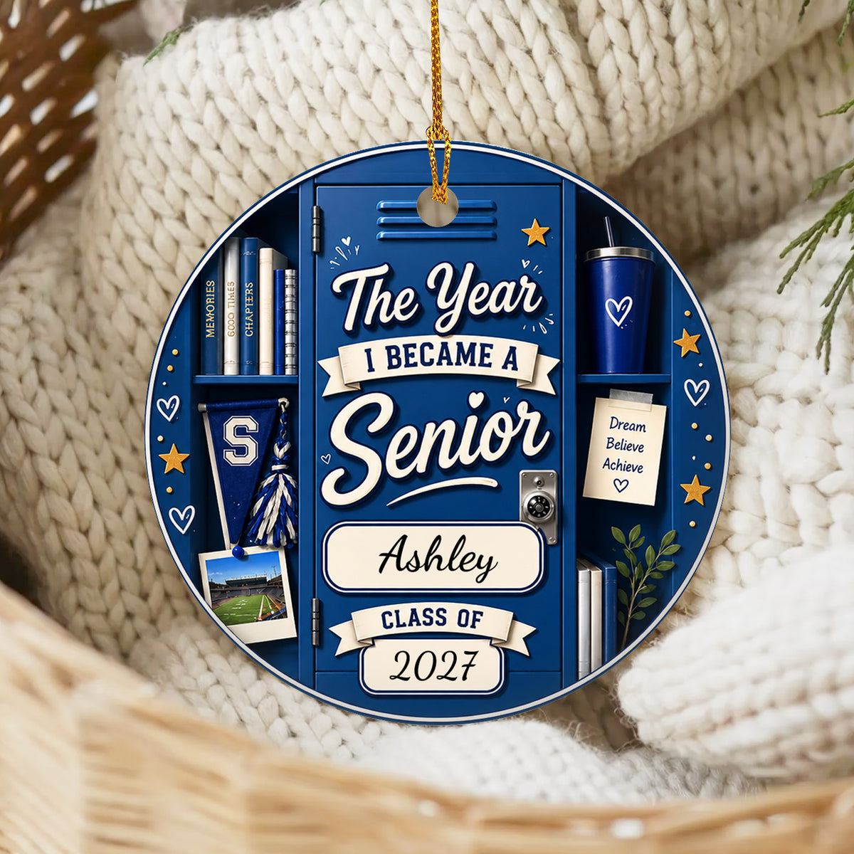 Personalized ceramic senior class ornament in blue resting on cream knit blankets in a woven basket