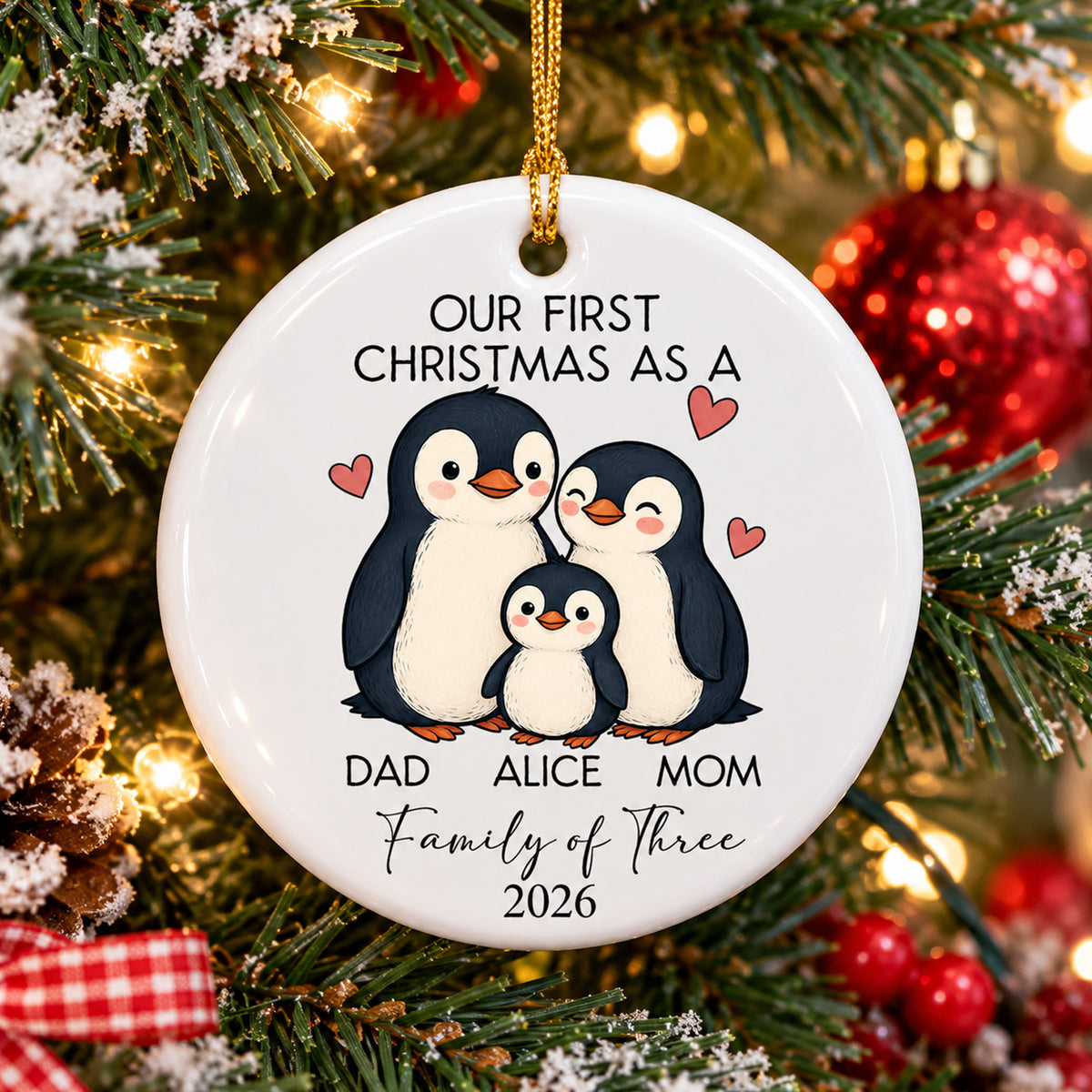 Personalized Ceramic Family Ornament with three penguins hanging on a snowy tree beside red baubles
