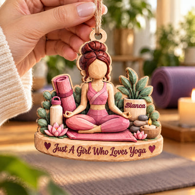 Personalized yoga wood ornament held by its twine loop in a hand, with a rolled yoga mat in the background