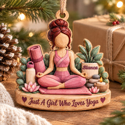 Personalized yoga wood ornament on a wooden surface beside a pine cone, wrapped gift and soft holiday lights